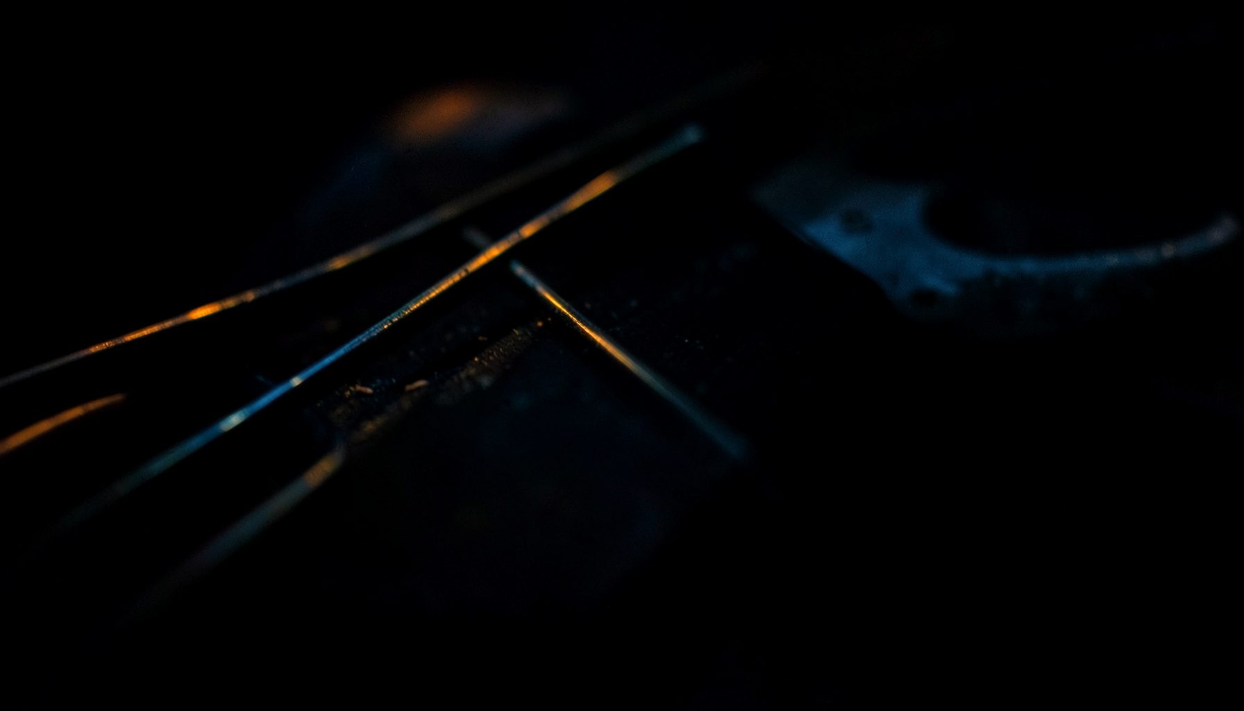 A dark, low-key photograph of violin strings in extreme close-up, deep black and navy shadows with a subtle amber highlight.