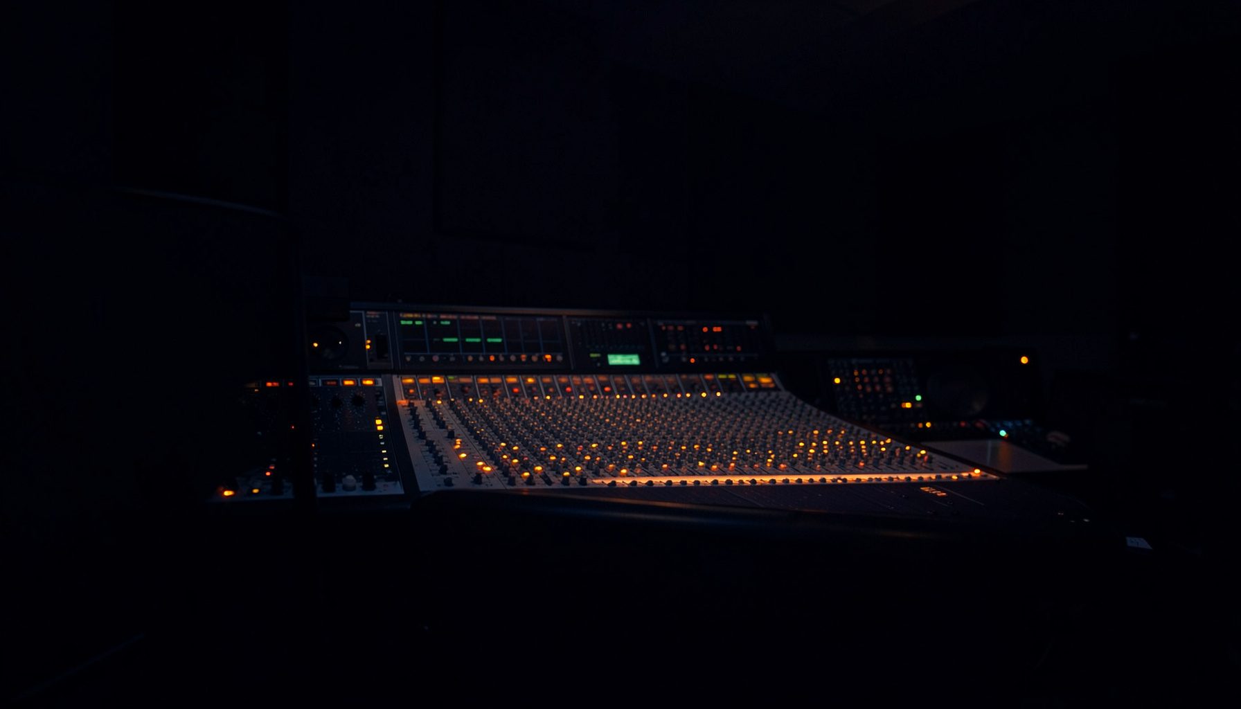 Dark atmospheric photograph of a dimly lit recording studio control room with mixing console, deep navy shadows and subtle amber glow