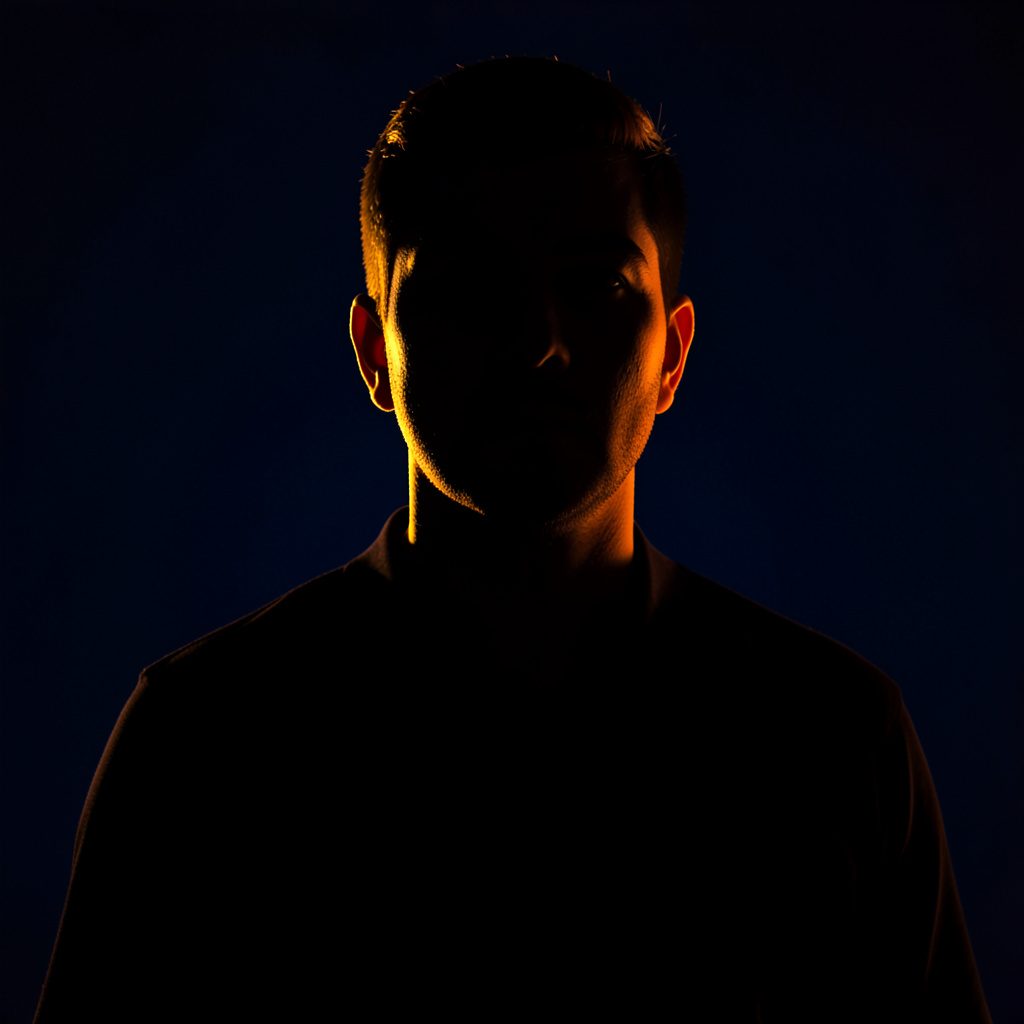 Dark low-key portrait photograph with deep navy background, warm amber rim light on a professional figure in shadow