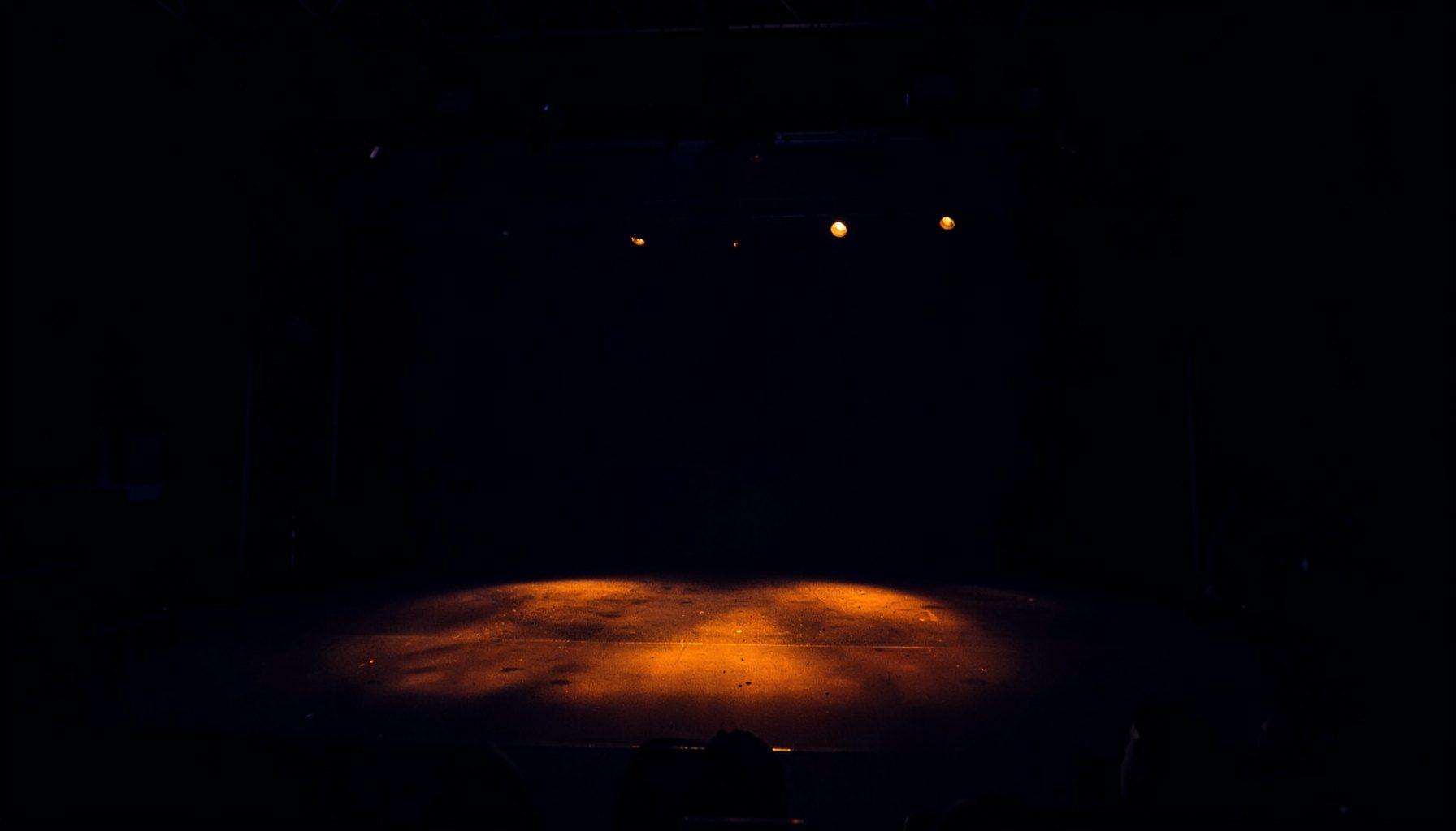 Dark atmospheric photograph of a concert stage with deep navy shadows and warm amber stage lights, empty stage before a performance